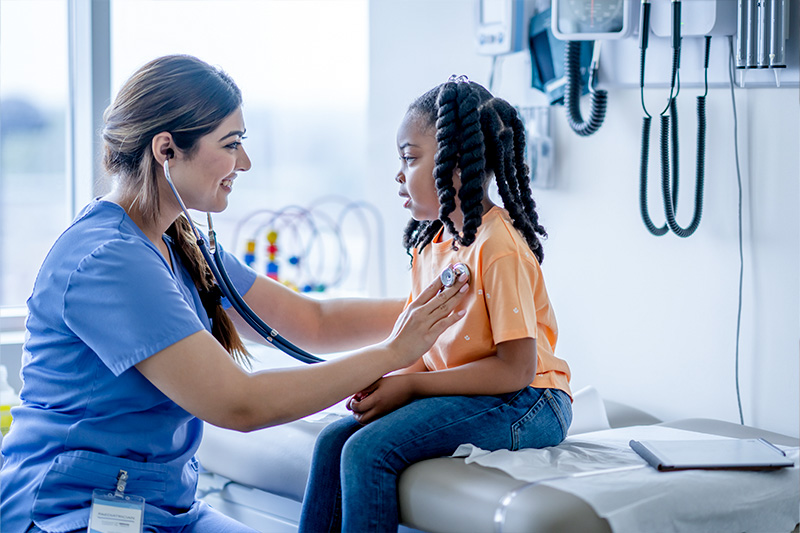 Picture of a child sitting on a medical table talking to a doctor while getting her heart checked.